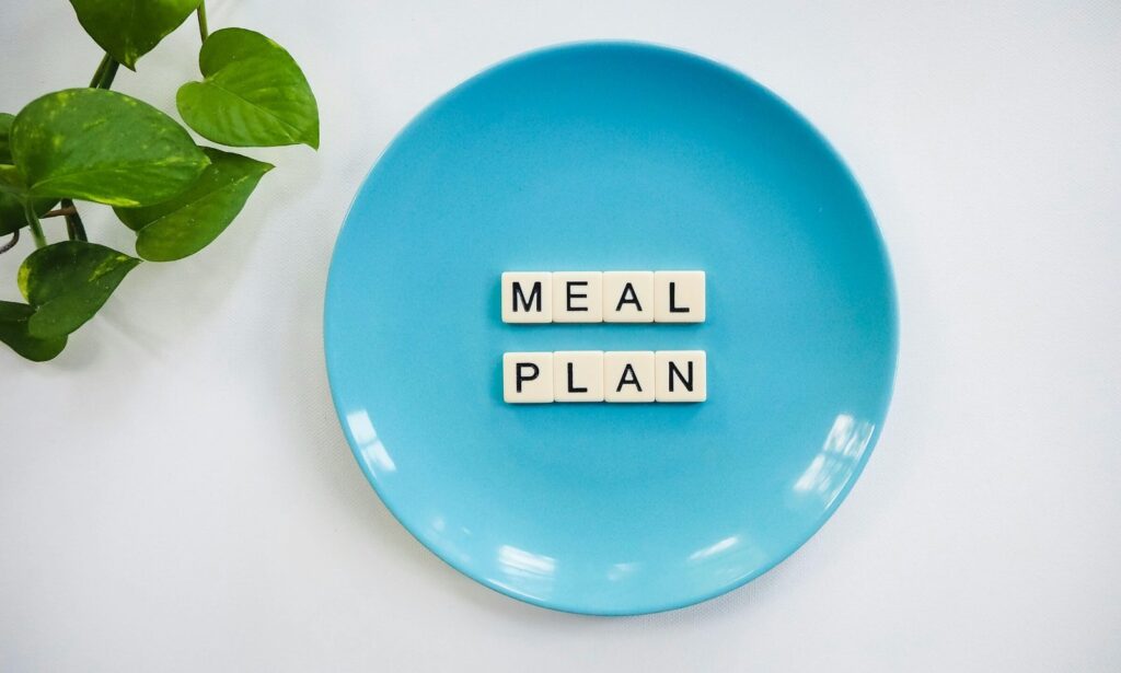 Innovative meal planning concept using alphabet tiles on a blue plate with green leaves.
